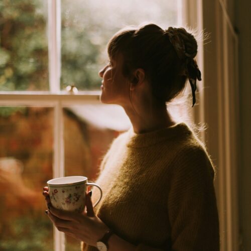 Woman with tea looking out window, representing quiet contemplation and healing journey in EMDR for sexual trauma