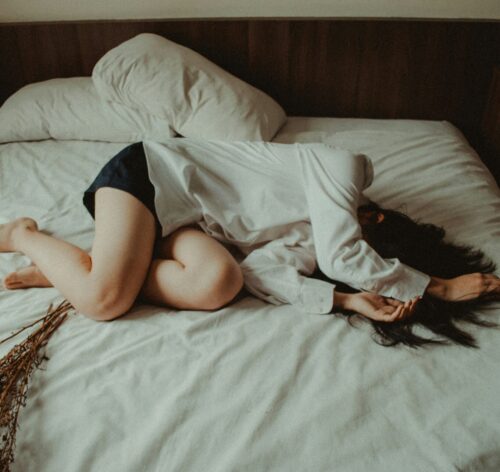 Woman lying on unmade bed with hair covering face, showing disconnection and distress from sexual traumas