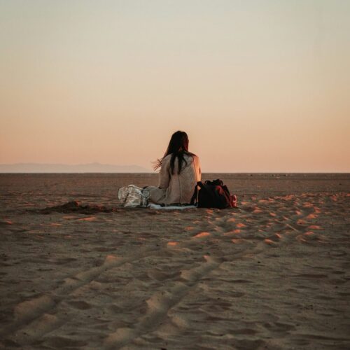 Woman sitting alone on beach at sunset, representing solitude and reflection on childhood trauma before EMDR treatment
